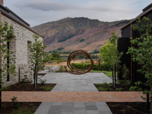 Outdoors at Milbrook house in Arrowtown with a view to the mountains. The Bernar Venet sculpture sits on Kandler sandstone paving with Terracotta bricks in the foreground.