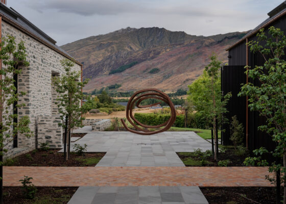Outdoors at Milbrook house in Arrowtown with a view to the mountains. The Bernar Venet sculpture sits on Kandler sandstone paving with Terracotta bricks in the foreground.